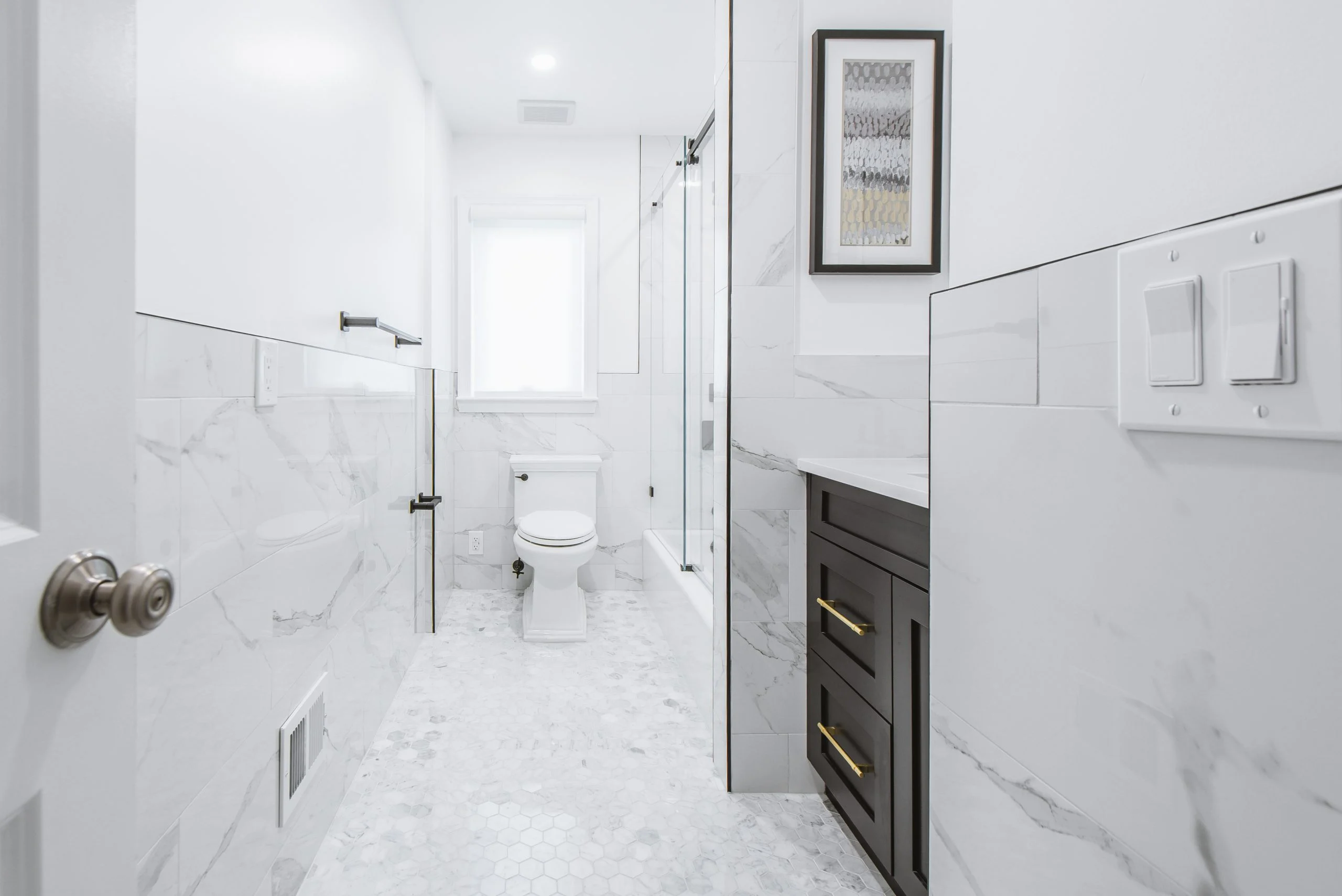 Modern white bathroom remodel with marble tile, glass shower, and dark vanity