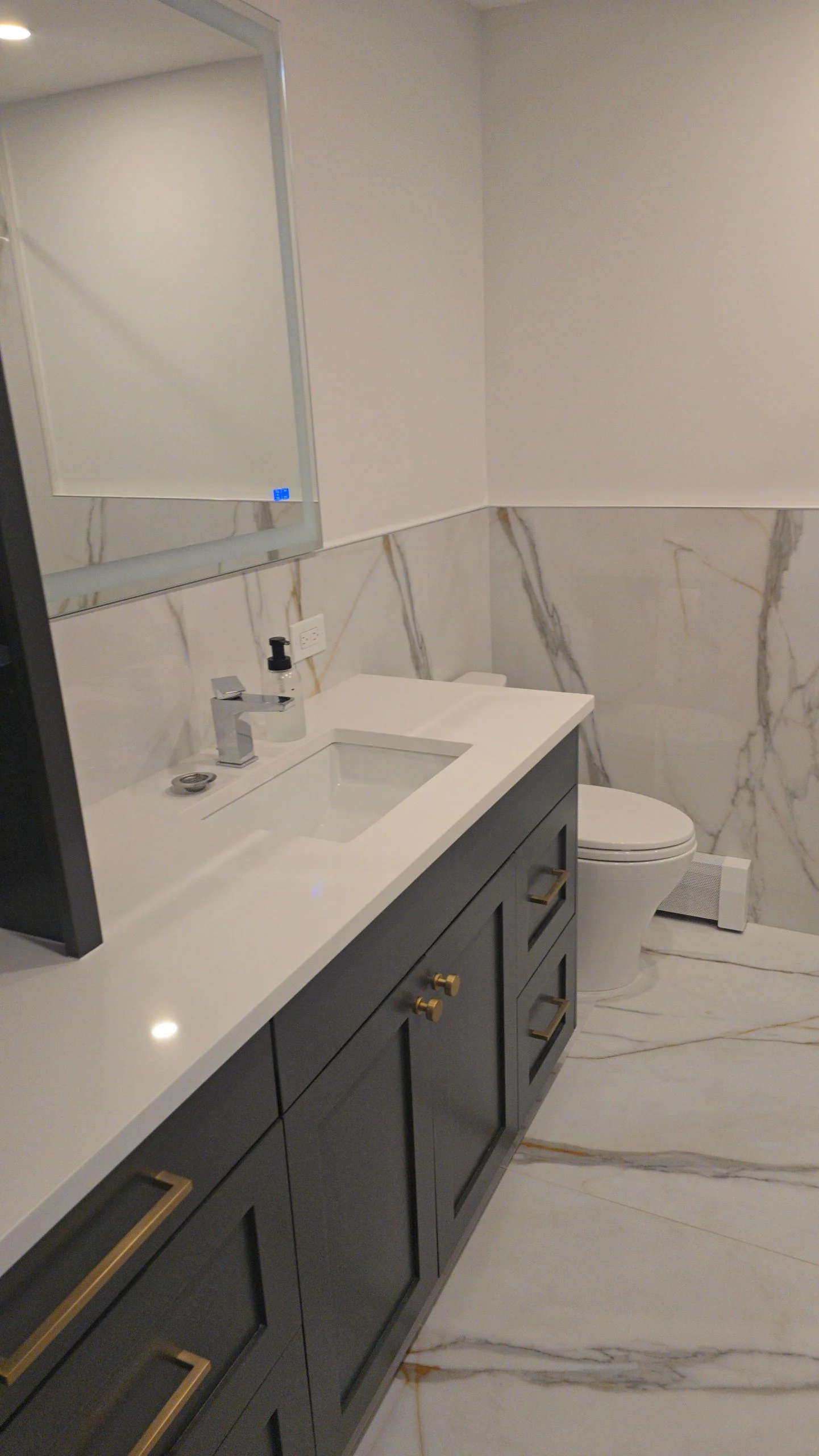 Bathroom remodel in New Rochelle NY with dark vanity, quartz countertop, and marble tile flooring