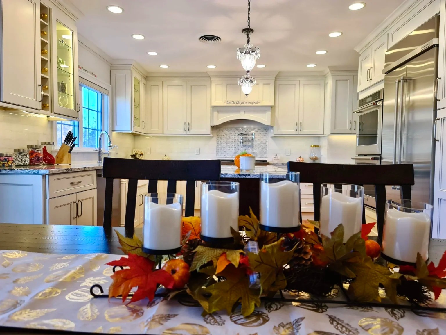 Dining table with candle centerpiece looking into white kitchen with island